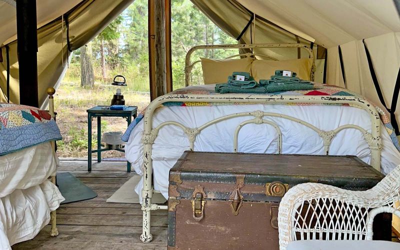Inside Bluebird wall tent with two beds, storage chest, chair, table and wood stove