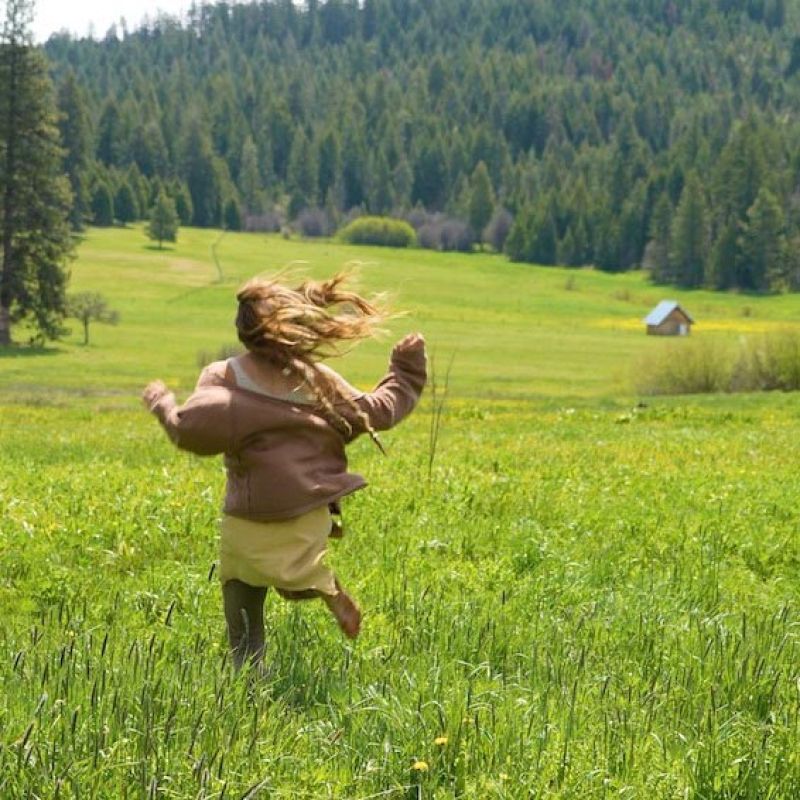 girl runs across meadow during farm stay vacation