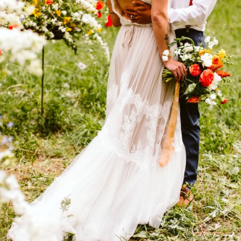 bride holding bouquet while groom embraces her during outdoor wedding ceremony
