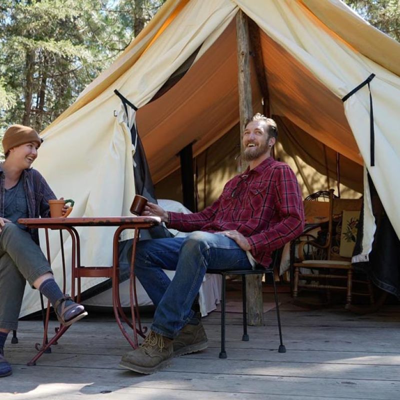campers enjoy coffee on the deck of their wall tent in the campground