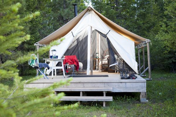campground luxury wall tent on raised platform with private deck, wood stove, comfortable bed and linens, chairs, and forest and meadow views